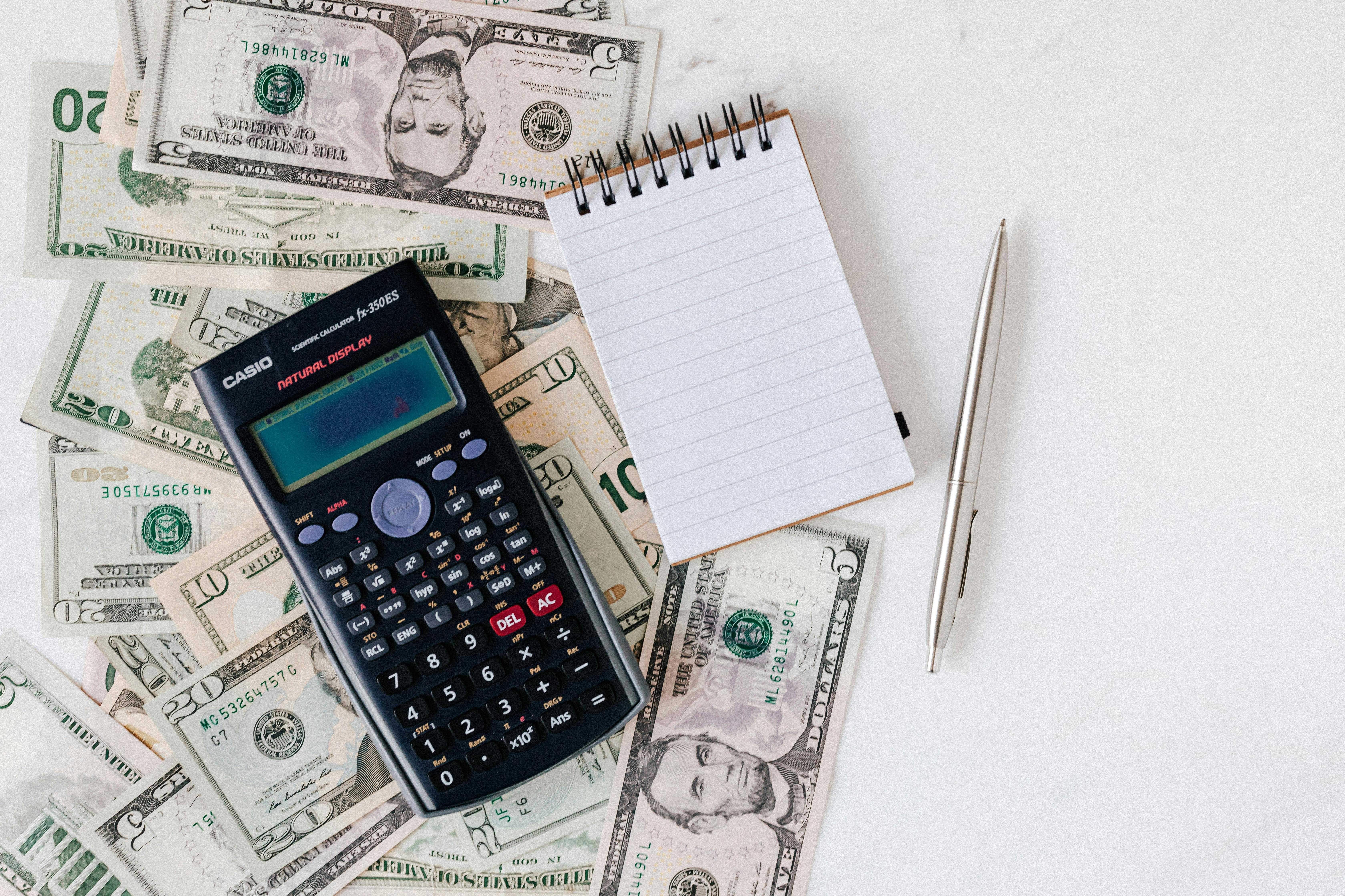 cash laid out with a calculator, notepad, and pen on top